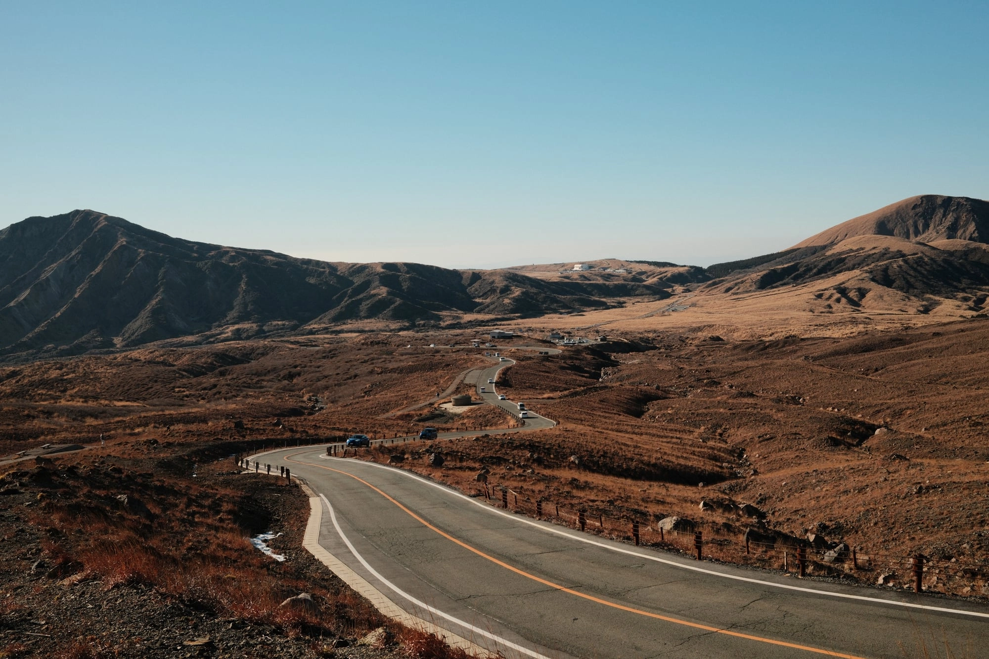 A curving mountain road cuts through golden volcanic grassland under a clear blue sky.