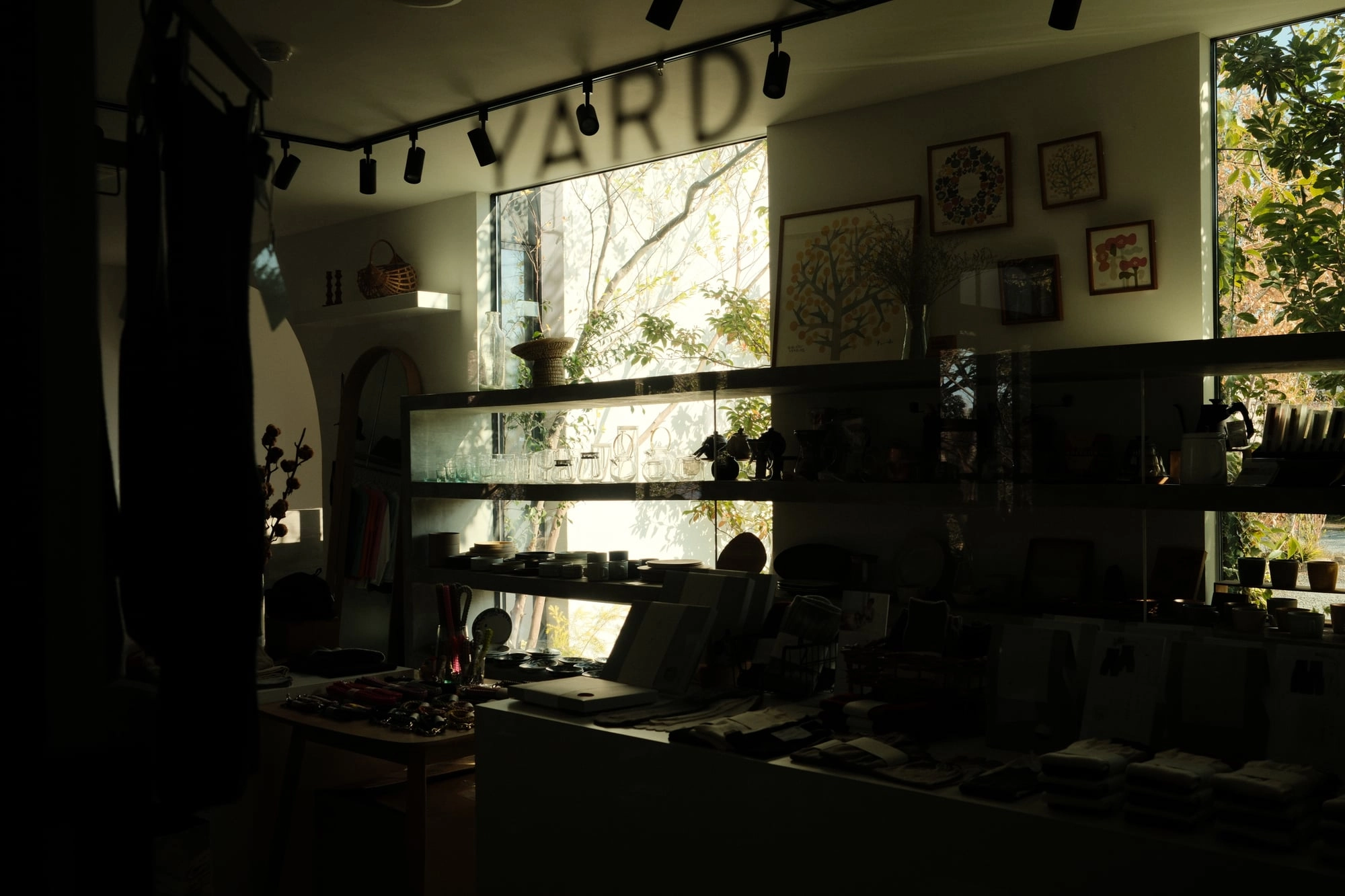 Shelves of glassware and framed art sit in a dim shop lit by a bright rear window.