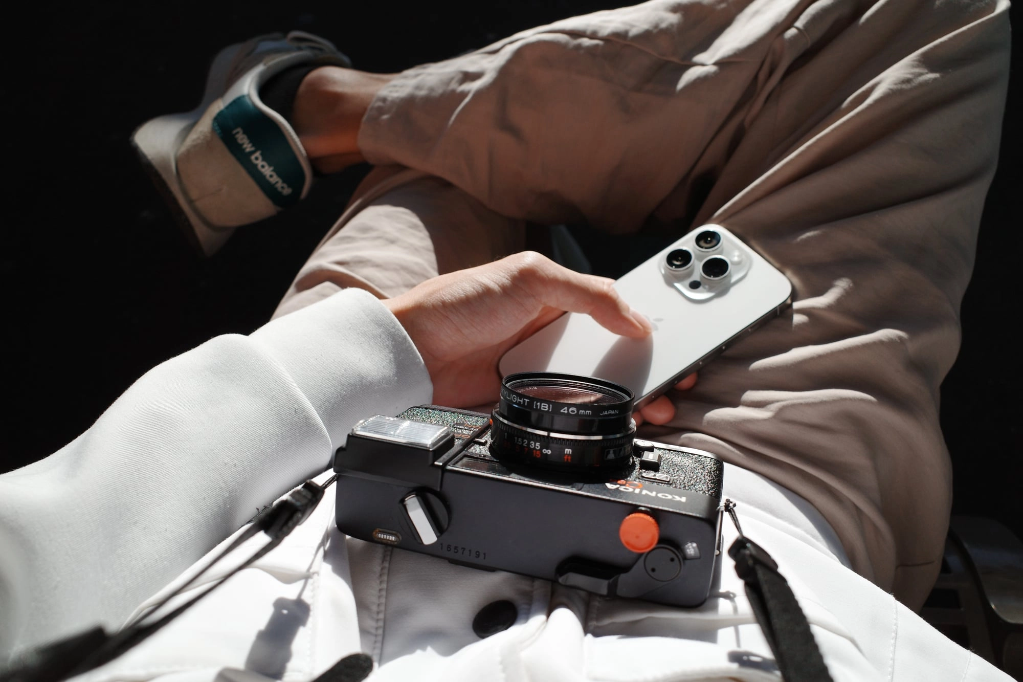 Sunlit hands hold a vintage film camera beside a smartphone, comparing old and new technology.