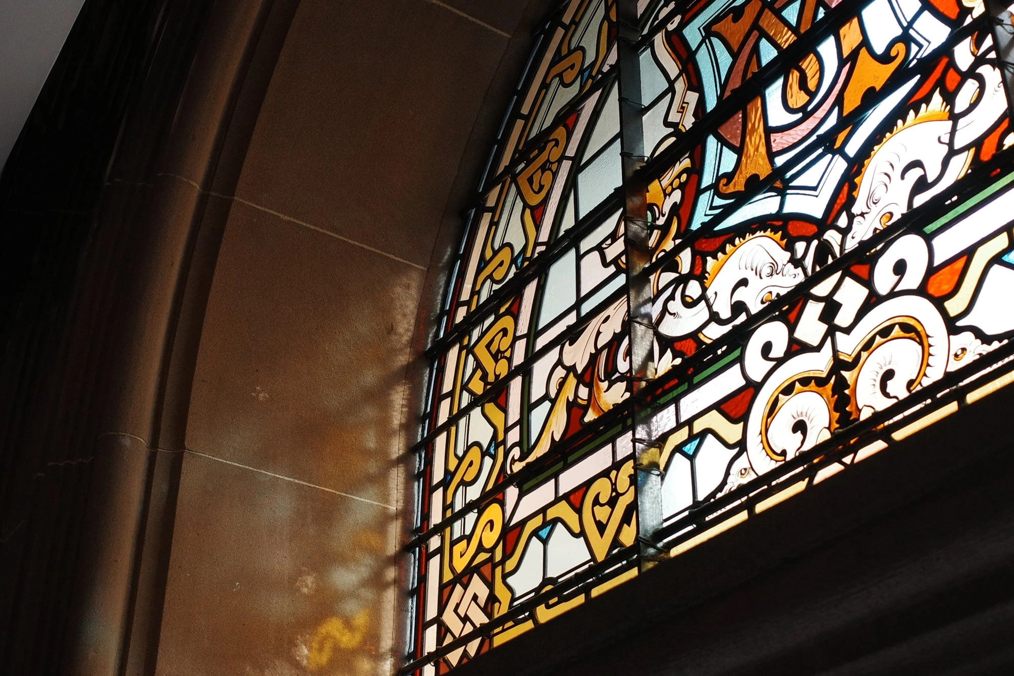 Sunlight glows through an angled stained-glass window patterned with intricate, colorful designs.